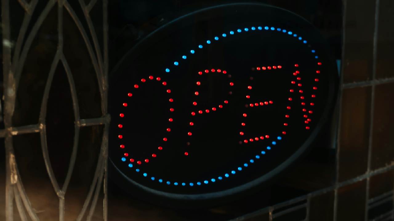 A brightly lit sign displayingc the word "OPEN" in neon letters, set against a dark background. The lights are arranged in a circular shape.